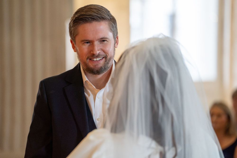 Groom smiling warmly at bride in white veil during wedding ceremony indoors.