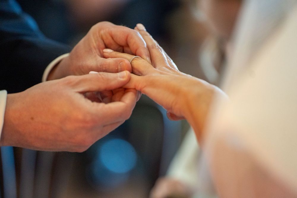 Close-up of groom placing wedding ring on brides finger during marriage ceremony.