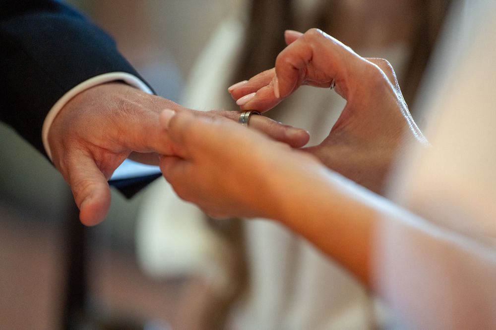 Close-up of a bride placing a wedding ring on the groom's finger during a marriage ceremony.