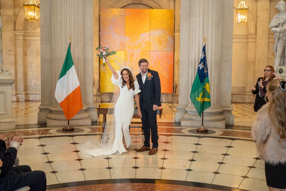 Newlywed couple celebrating at Dublin City Hall wedding ceremony with Irish flag in background.