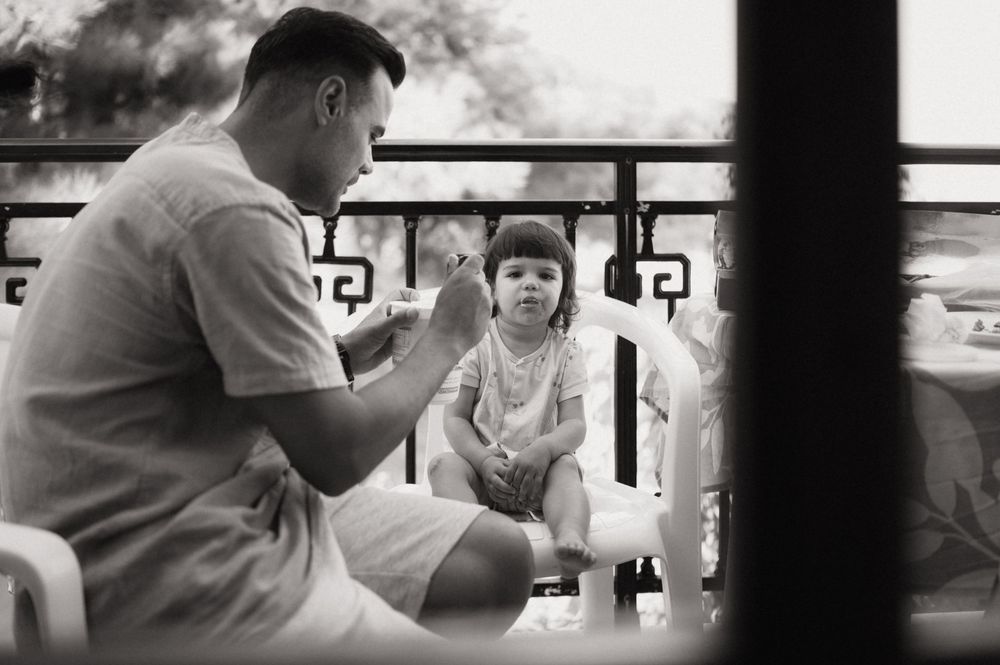 Black and white photo of a father talking to his young daughter on a balcony.