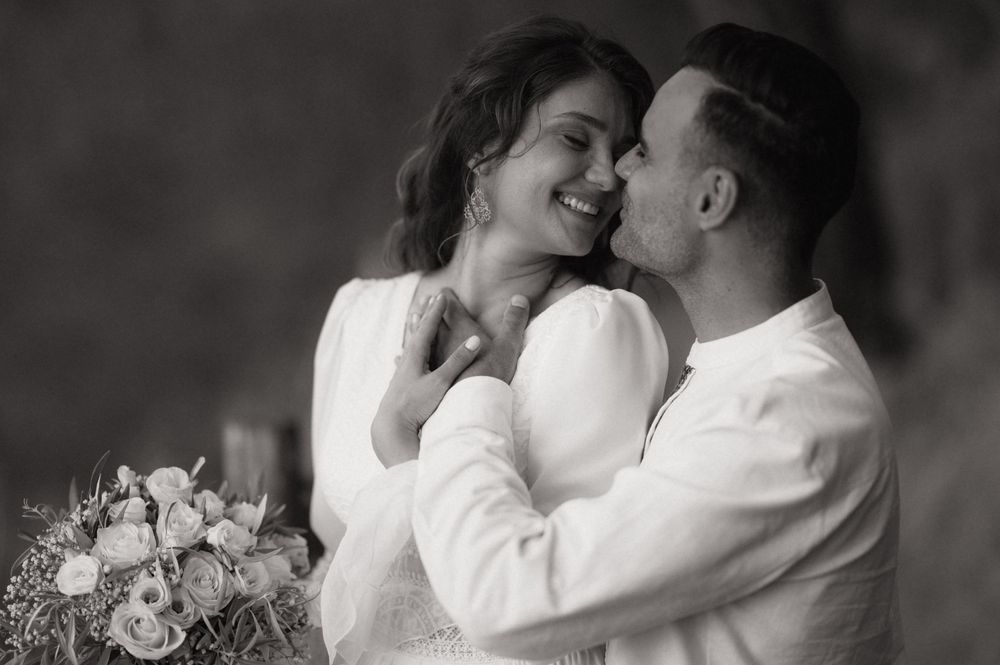 Black and white wedding photo of a smiling bride holding bouquet and groom in white shirt sharing a romantic moment.