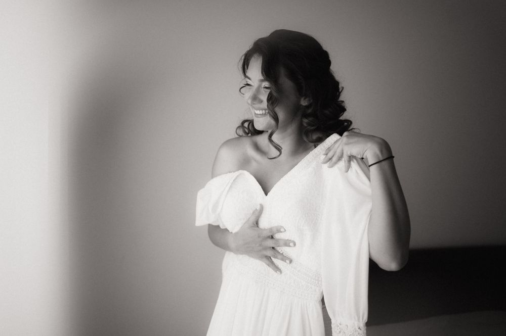 Elegant bride in white off-shoulder gown poses gracefully in black and white portrait photography.