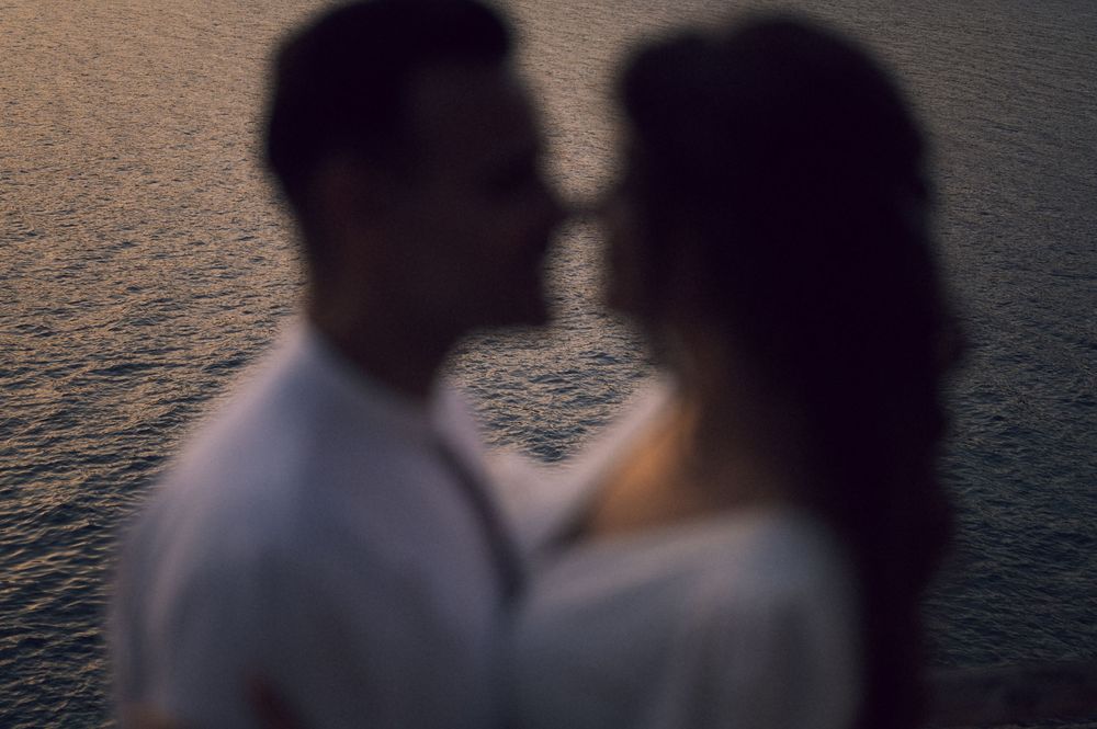 Romantic couple sharing an intimate moment near shimmering water at dusk in a soft focus portrait.