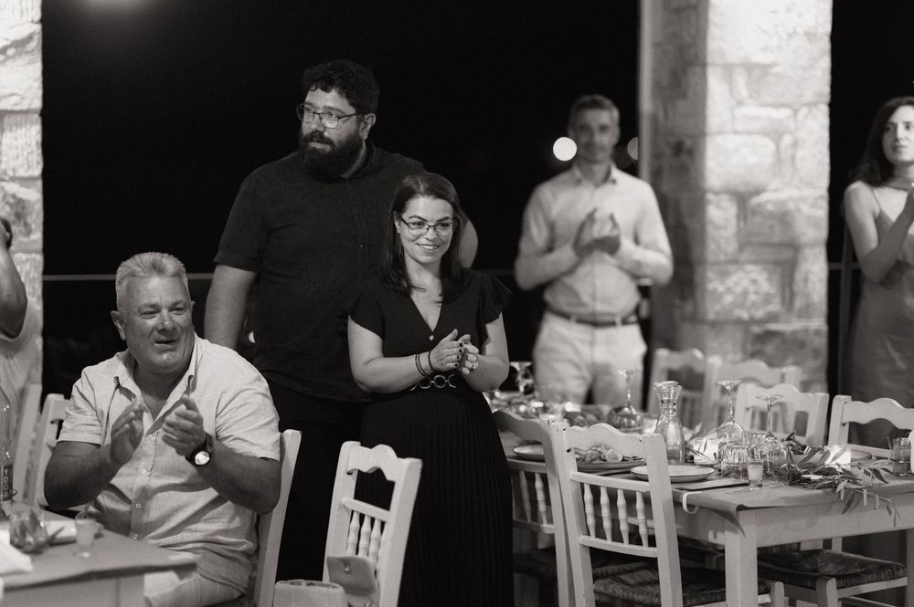 Black and white photo of guests gathered at an outdoor evening dinner party, with a couple standing together in the center.