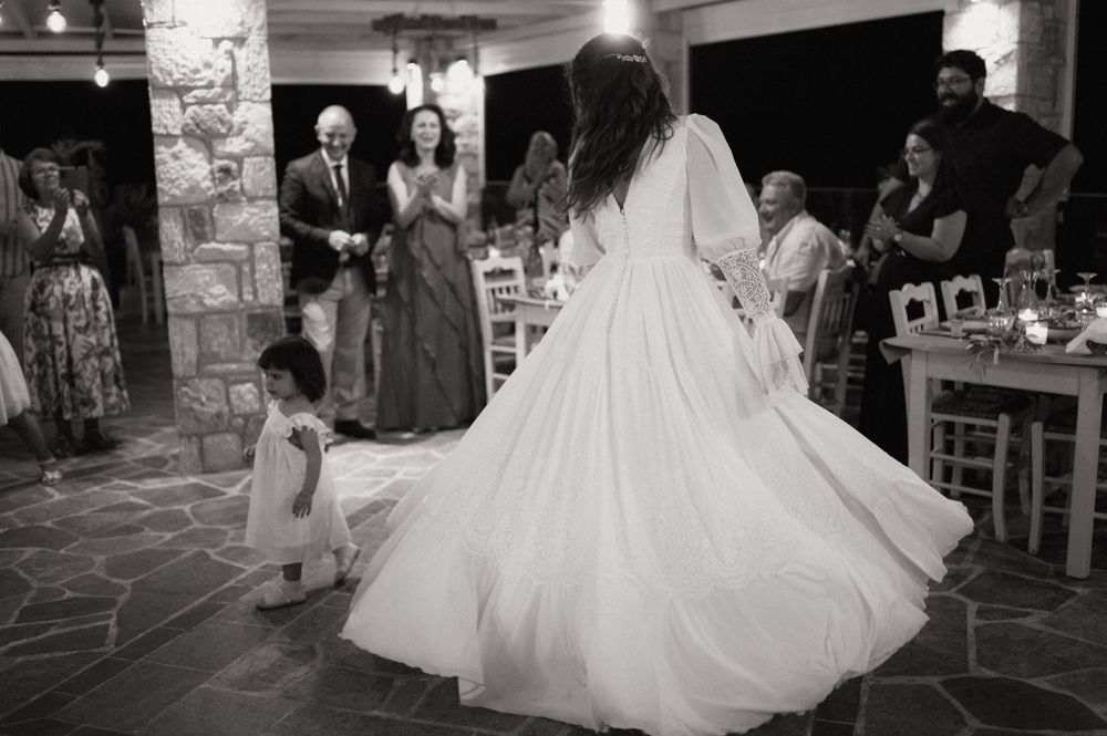 Bride twirling in white gown with flower girl at wedding reception, guests applauding in black and white photo.
