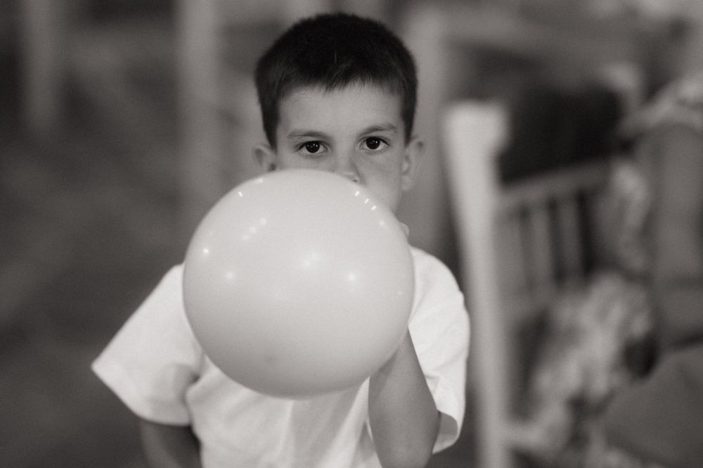 Black and white photo of a young boy blowing up a balloon at a party.