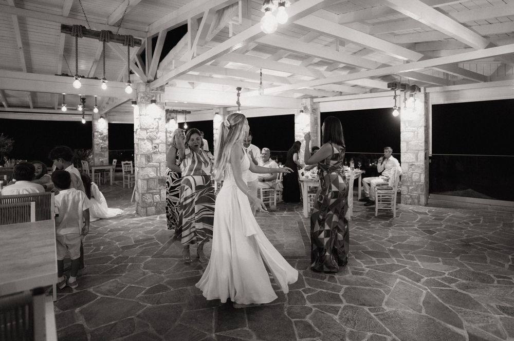 Bride dancing with guests at an outdoor wedding reception under string lights on a stone patio.