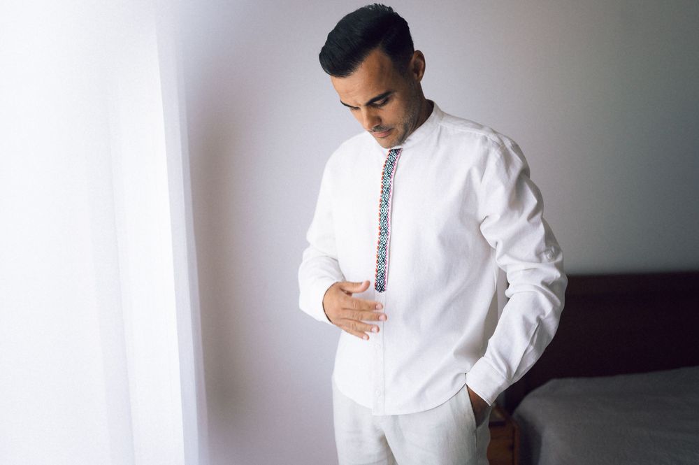 Man in white embroidered shirt adjusting his outfit while getting ready for a wedding ceremony.