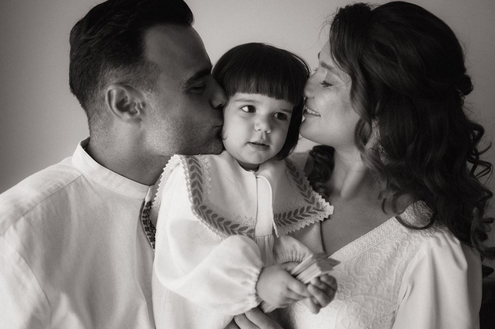 Black and white photo of parents kissing their toddler on cheeks, family portrait with warm expressions.