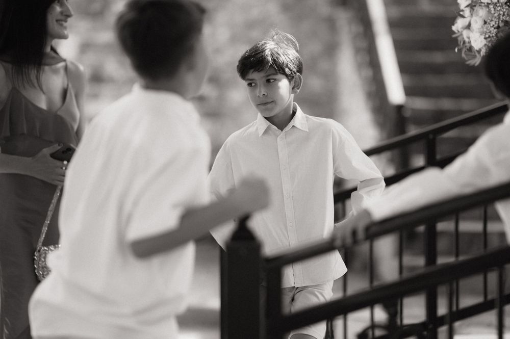 Black and white photo of a young boy in a white shirt standing near railing at an outdoor event.