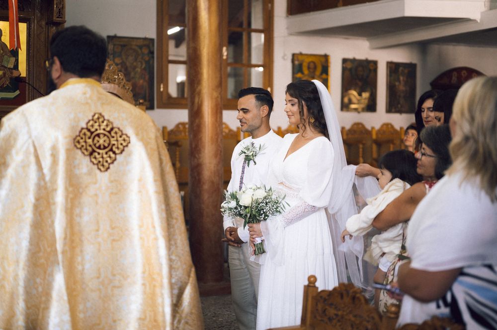 Bride and groom stand at the altar during an Orthodox church wedding ceremony, bride holding white floral bouquet.
