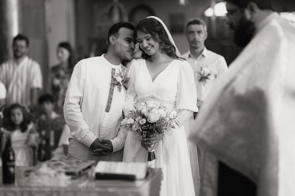 Black and white wedding photo of smiling bride and groom during ceremony, bride holding bouquet.