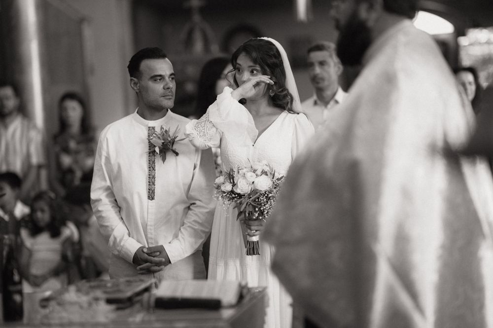 Black and white wedding ceremony photo of bride and groom standing at altar with officiant in elegant church setting.