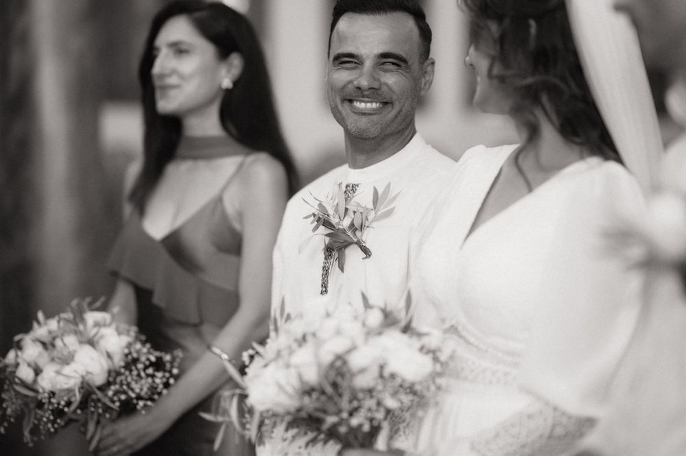 Black and white wedding photo of smiling groom with bridesmaids holding bouquets at elegant ceremony.