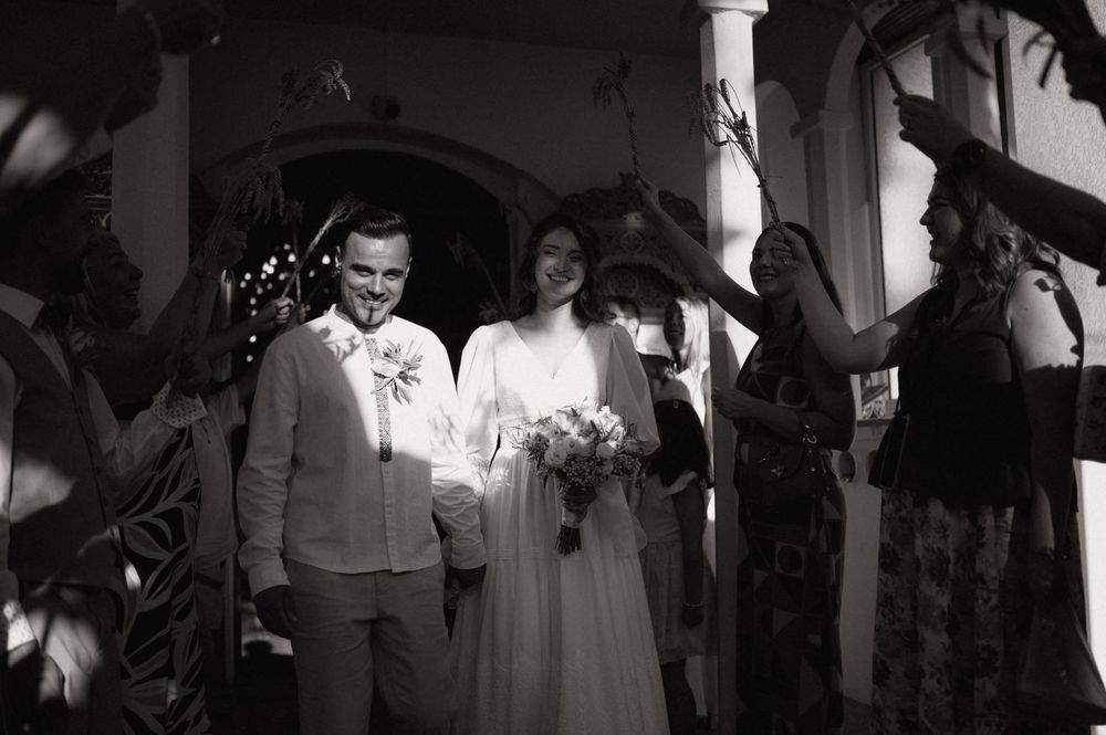 Black and white photo of a smiling newlywed couple exiting a ceremony as guests celebrate around them.