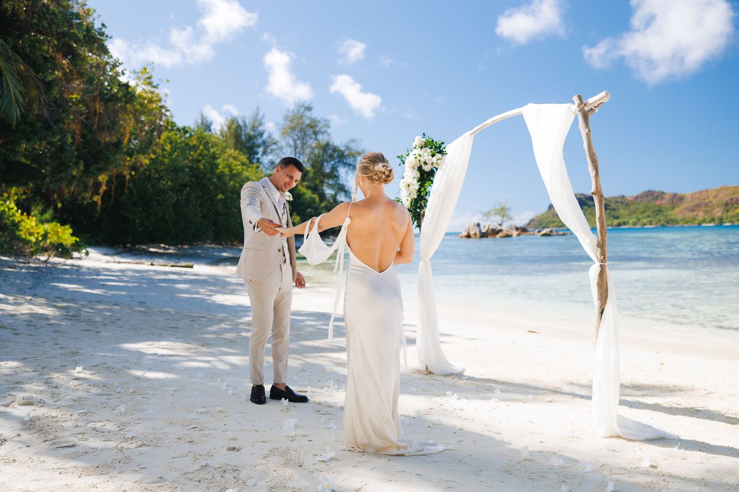 Bride and groom exchanging vows at a decorated beach wedding arch with turquoise ocean backdrop.