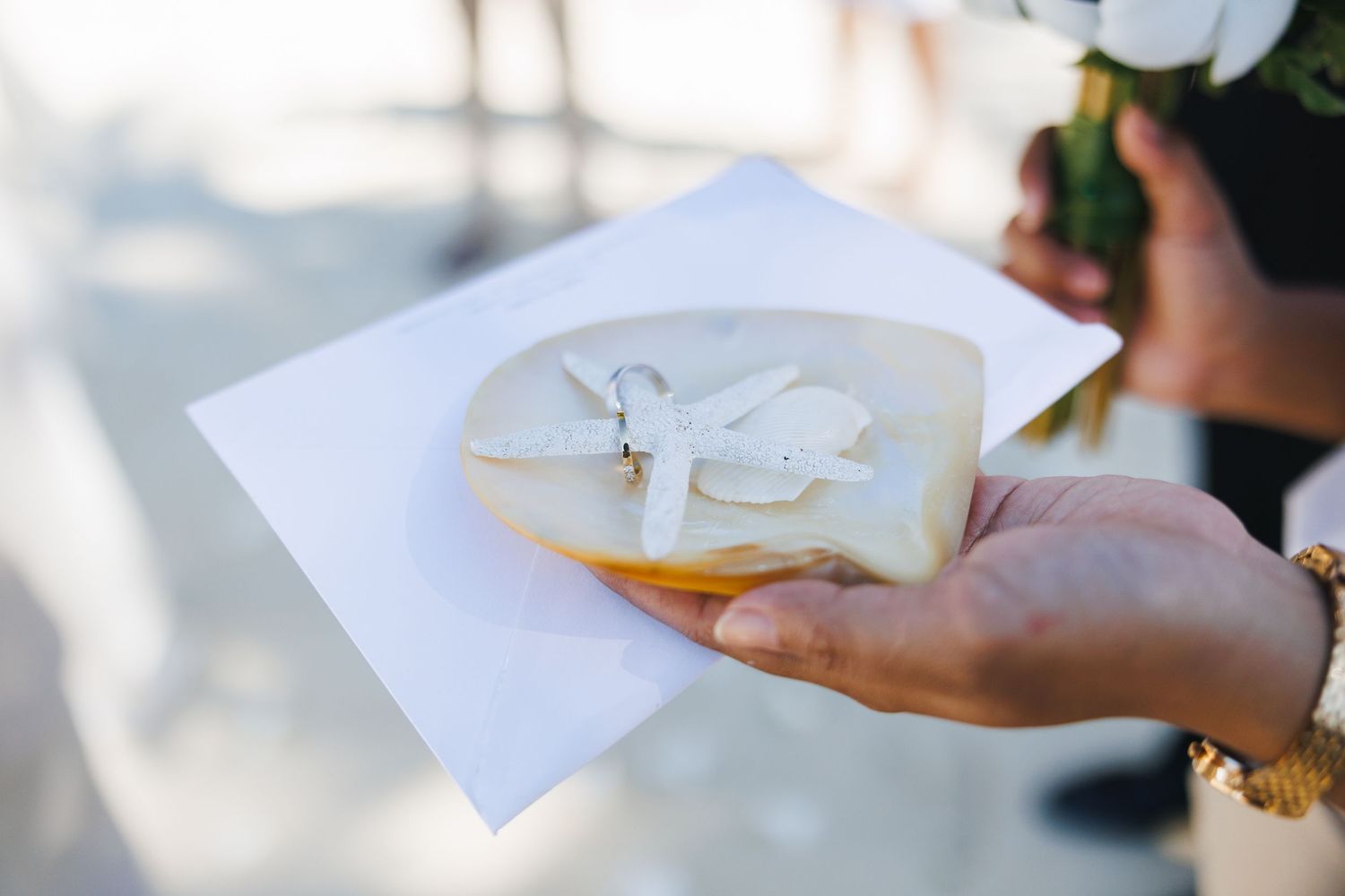 Wedding rings displayed on a tropical leaf with a white envelope during a beach ceremony.