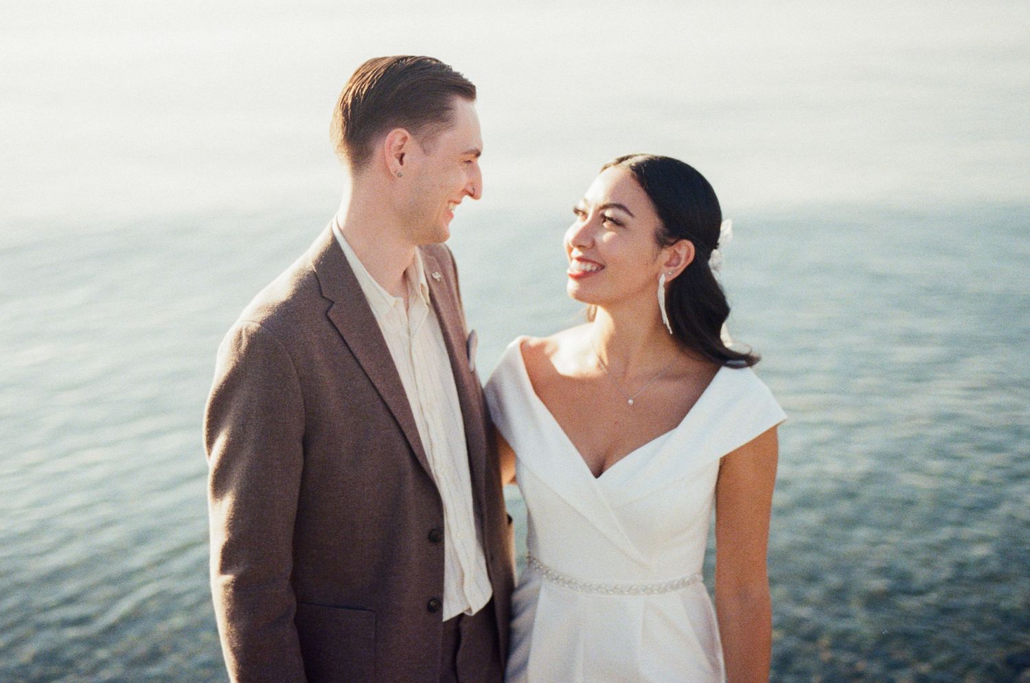 35 mm film photo of bride and groom smiling at each other beside the ocean