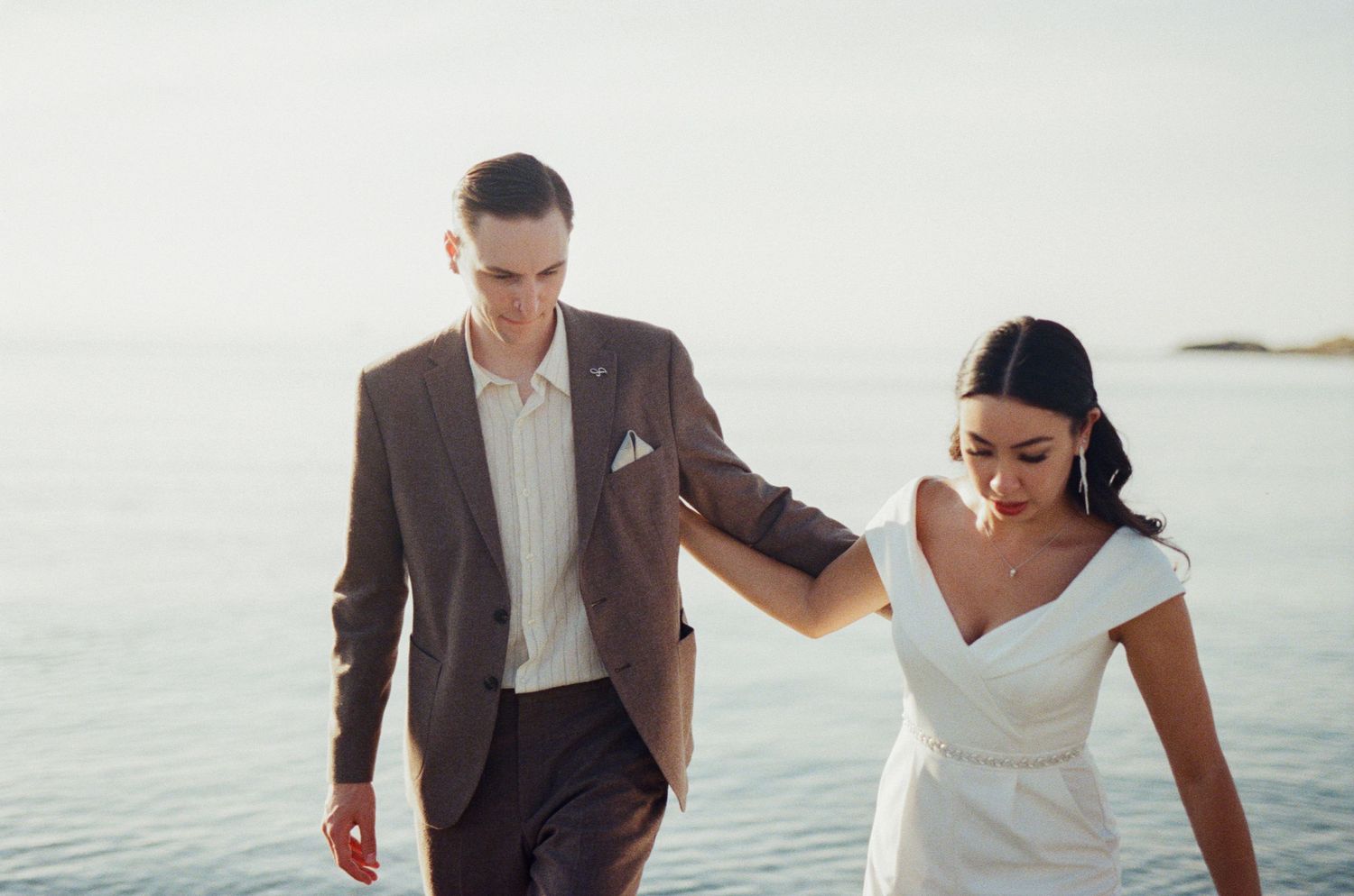 35 mm film photo of bride and groom walking along the shore beside the ocean