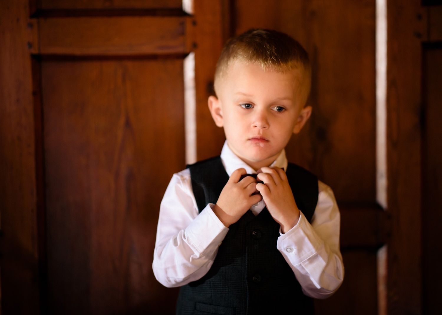 Worsley Court House Salford wedding photography boy adjusting bow tie against wood panelling