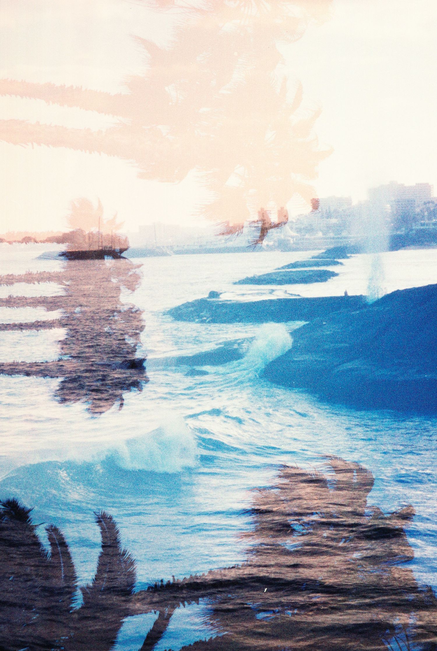 Double exposure photograph of ocean waves and a coastal cityscape in soft blue and peach tones.