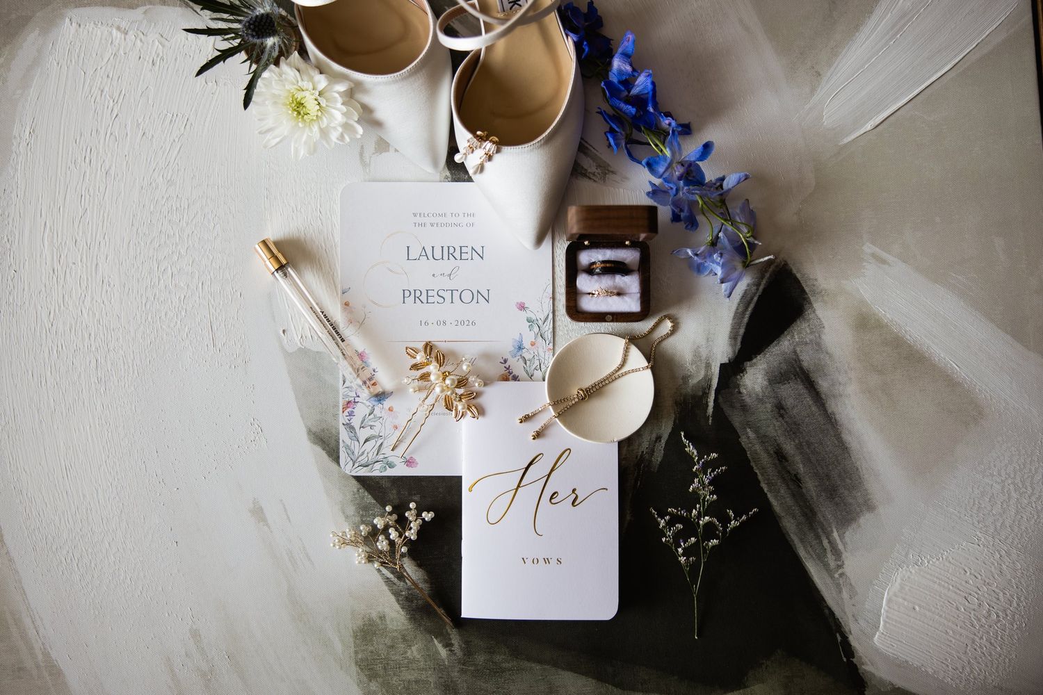 Wedding flat lay with Lauren and Preston invitation, ivory heels, ring box, pearl hair pins and her vows book