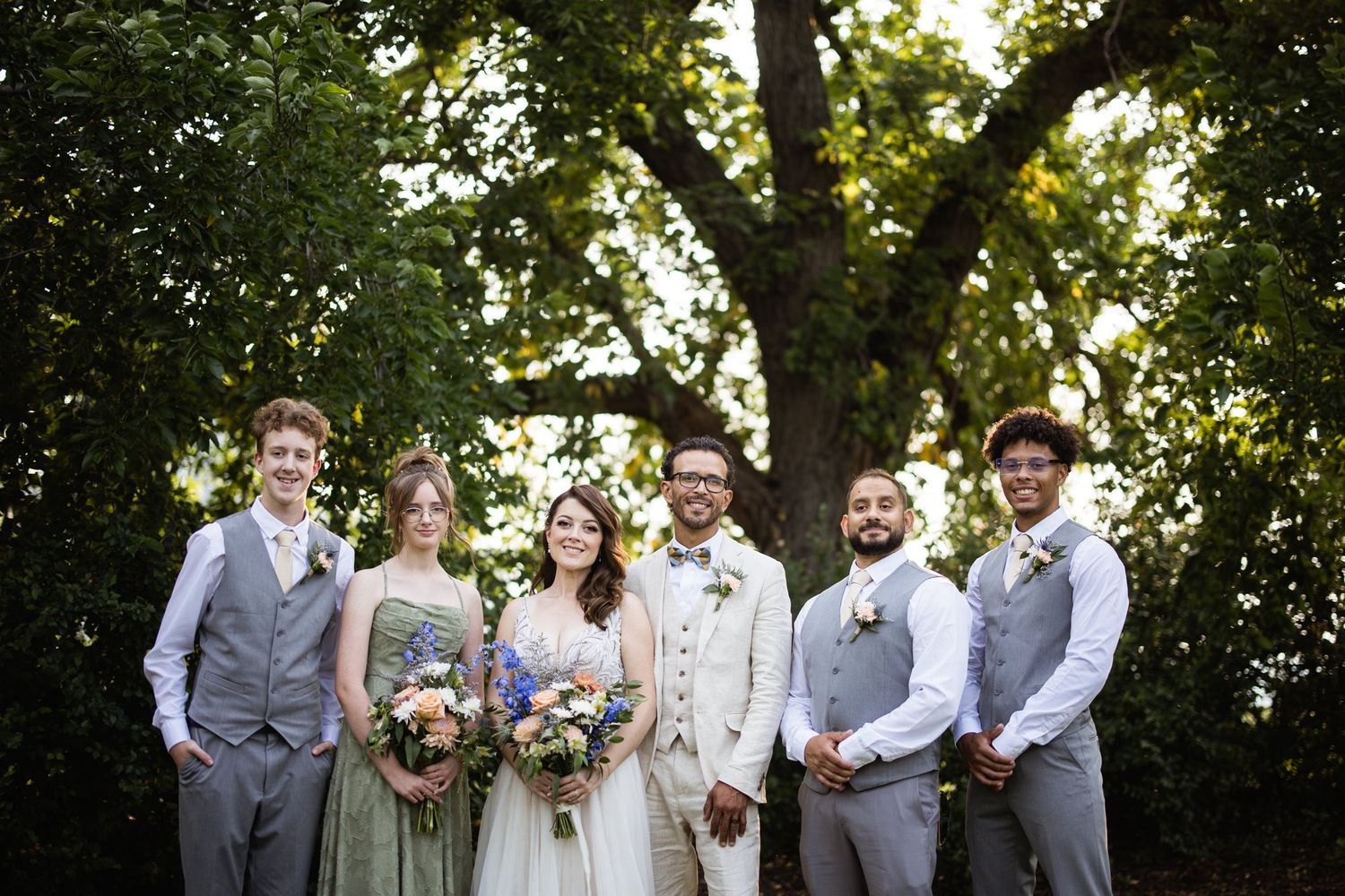 Calgary wedding party in sage and grey standing under a large leafy tree