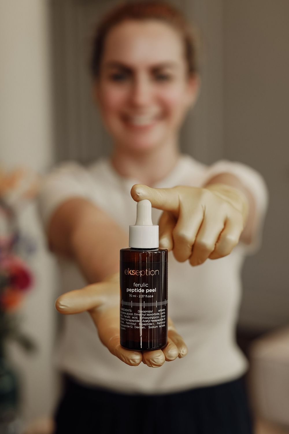 Smiling woman holding a dark bottle of Elixseption peptide peel serum with dropper toward camera.