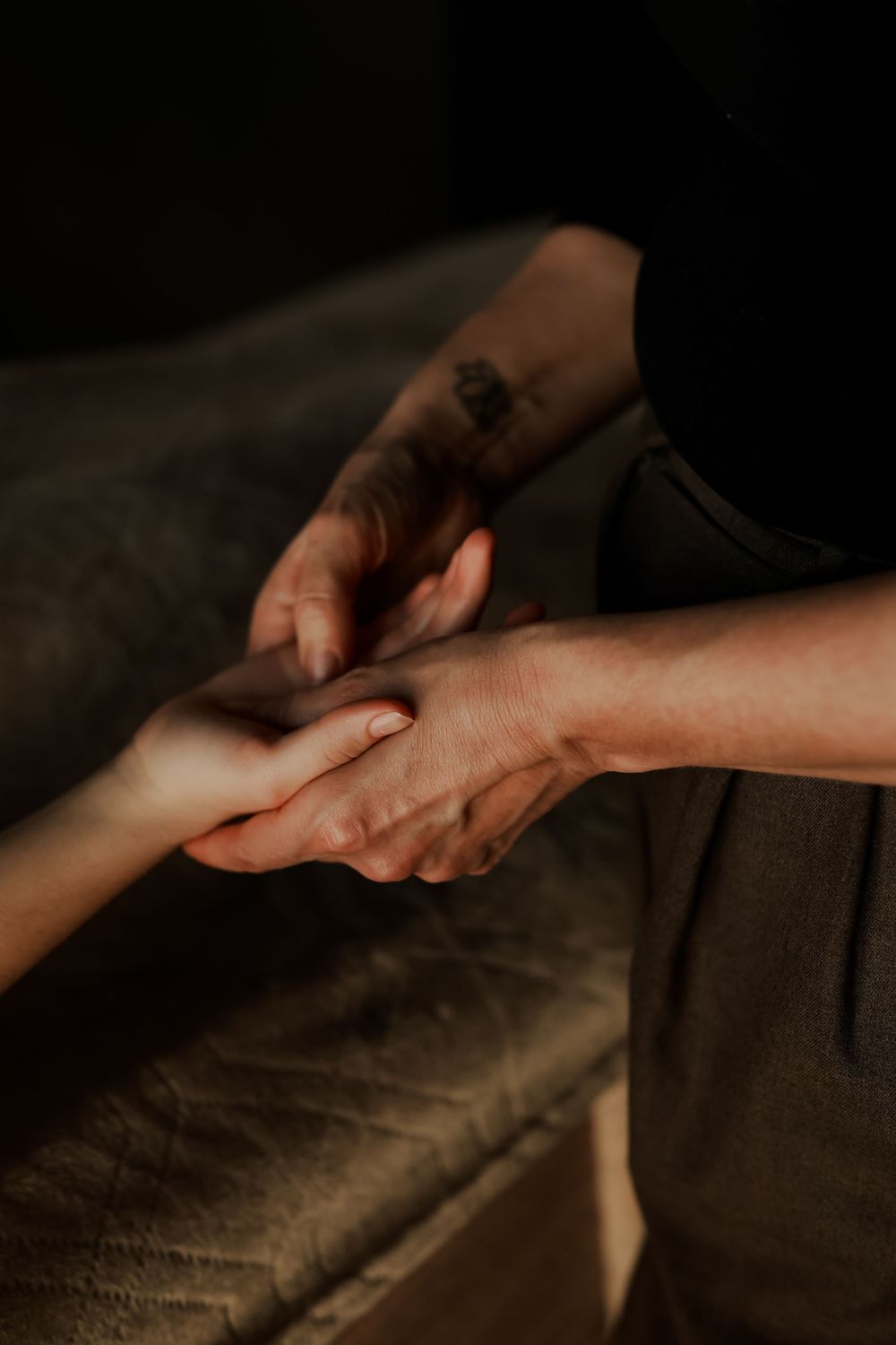 A massage therapist with a tattoo gently holds a client's hand during a relaxing hand massage therapy session.