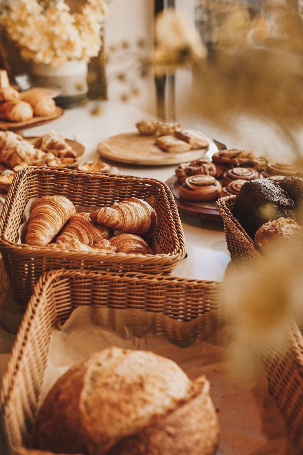 Wicker baskets filled with fresh croissants and pastries displayed on a bakery counter with cinnamon rolls and bread.