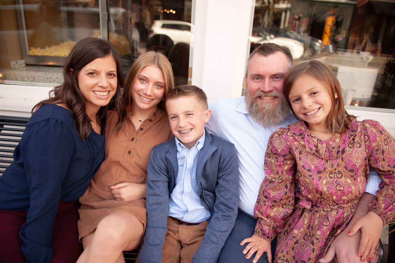 Family of five smiling together outdoors, including parents, two girls, and a boy in casual attire.
