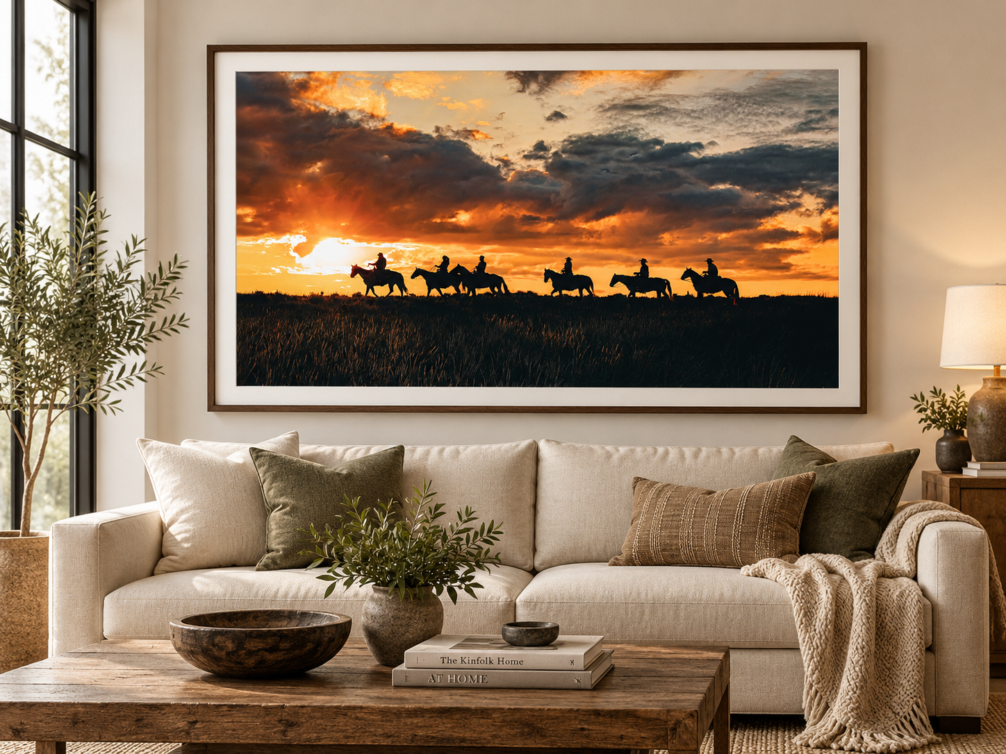 Silhouette of cowboys on horseback riding across a golden sunset landscape, framed art print displayed in a modern living room.