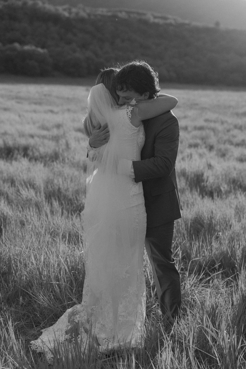 Black and white photo of bride and groom embracing in a field, sharing a tender moment on their wedding day.