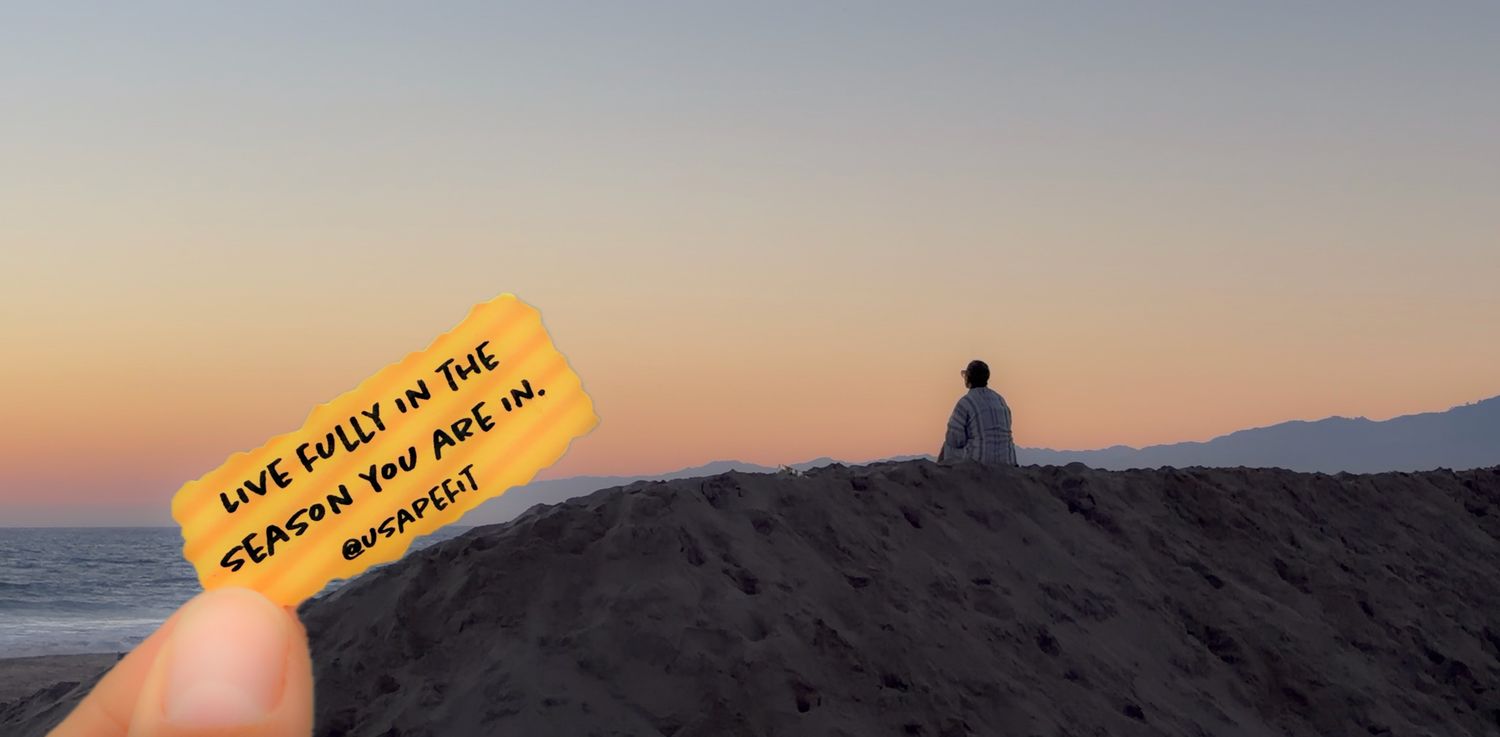 Hand holding a yellow note card with inspirational quote at sunset beach with silhouette sitting on sand dune.