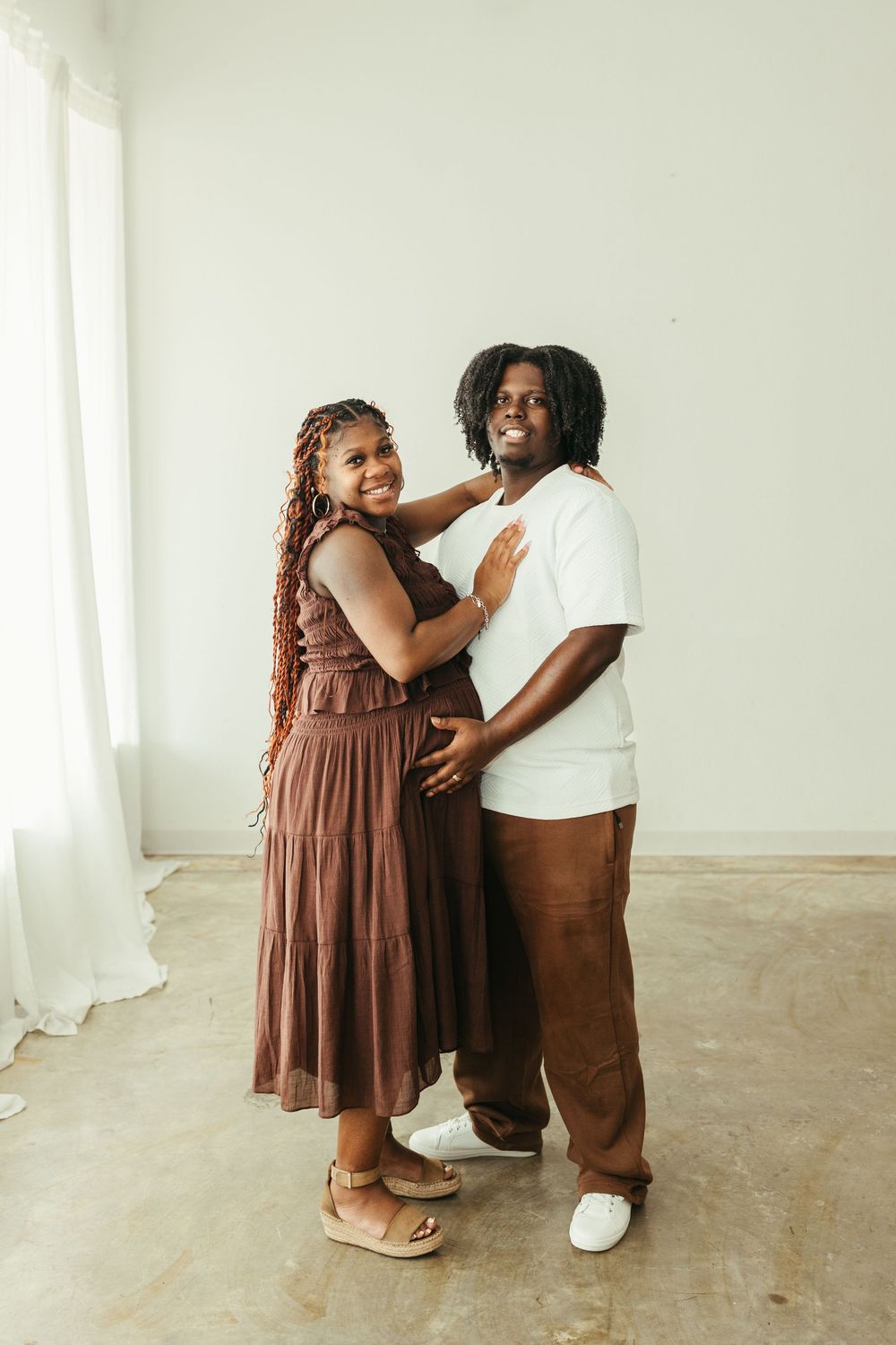 Happy Black couple embracing and smiling together in a bright white studio, woman in brown dress.