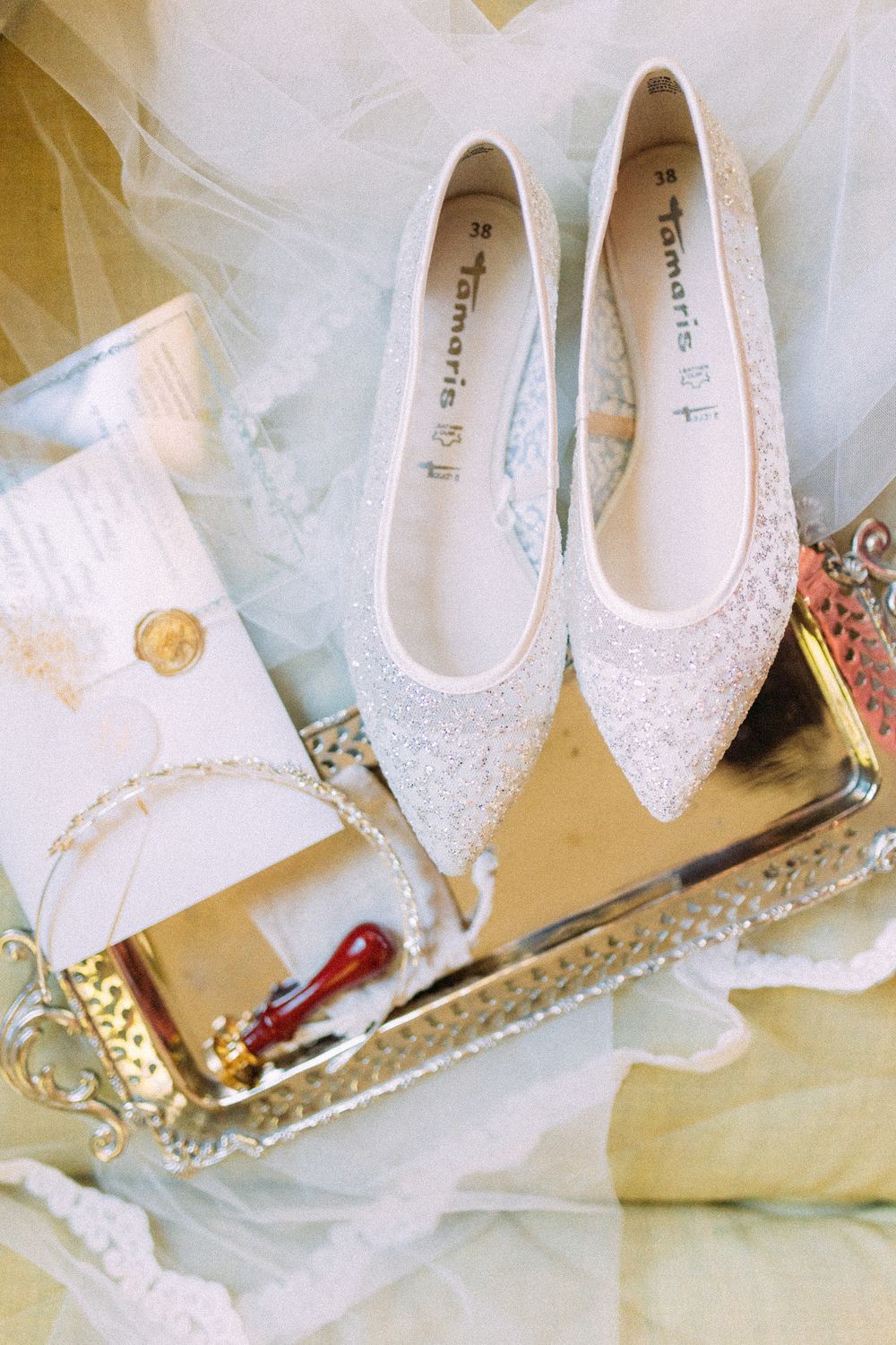 Elegant Tamaris bridal flat shoes adorned with glitter on a gold tray with wax seal stationery and veil.