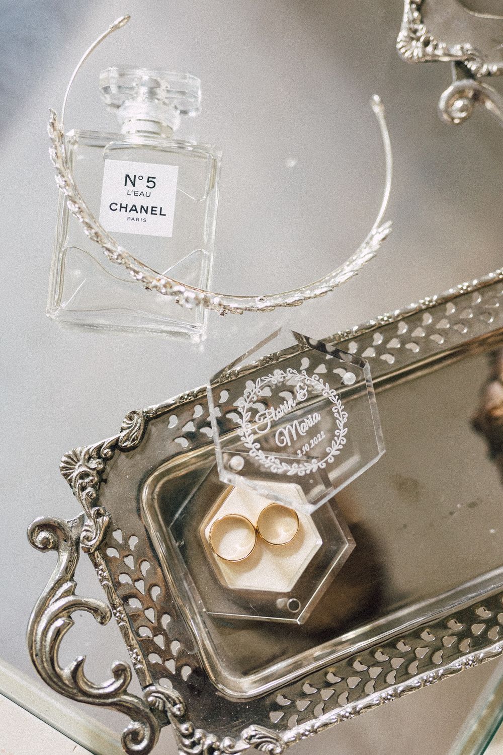 Chanel No.5 L'eau perfume bottle, gold wedding rings in hexagon box, and hair vine on ornate silver mirrored tray.