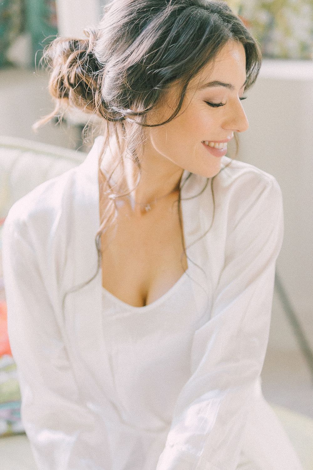 Smiling young woman with dark updo hair wearing a white shirt and camisole, looking down gracefully.
