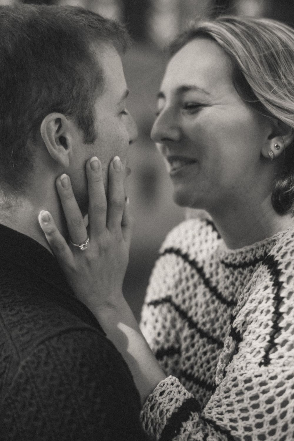 Black and white photo of a smiling woman tenderly holding a man's face close to hers in a romantic moment.