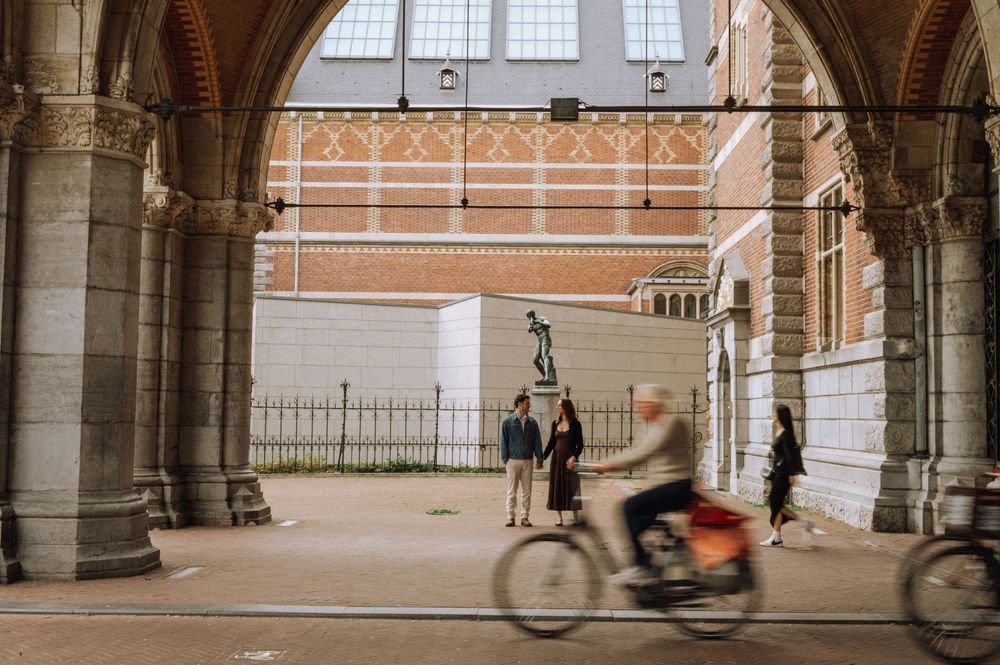 Cyclist riding through an arched passage of the Rijksmuseum in Amsterdam with pedestrians and brick facade in background.