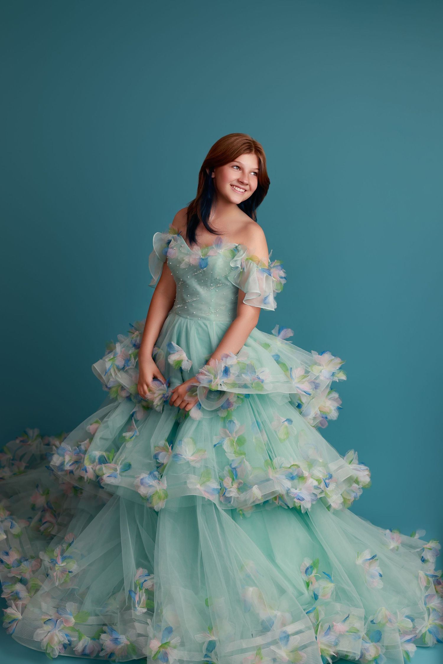 Smiling girl in a mint green tiered tulle ball gown with floral appliques, posing against a teal studio background in Covington, GA