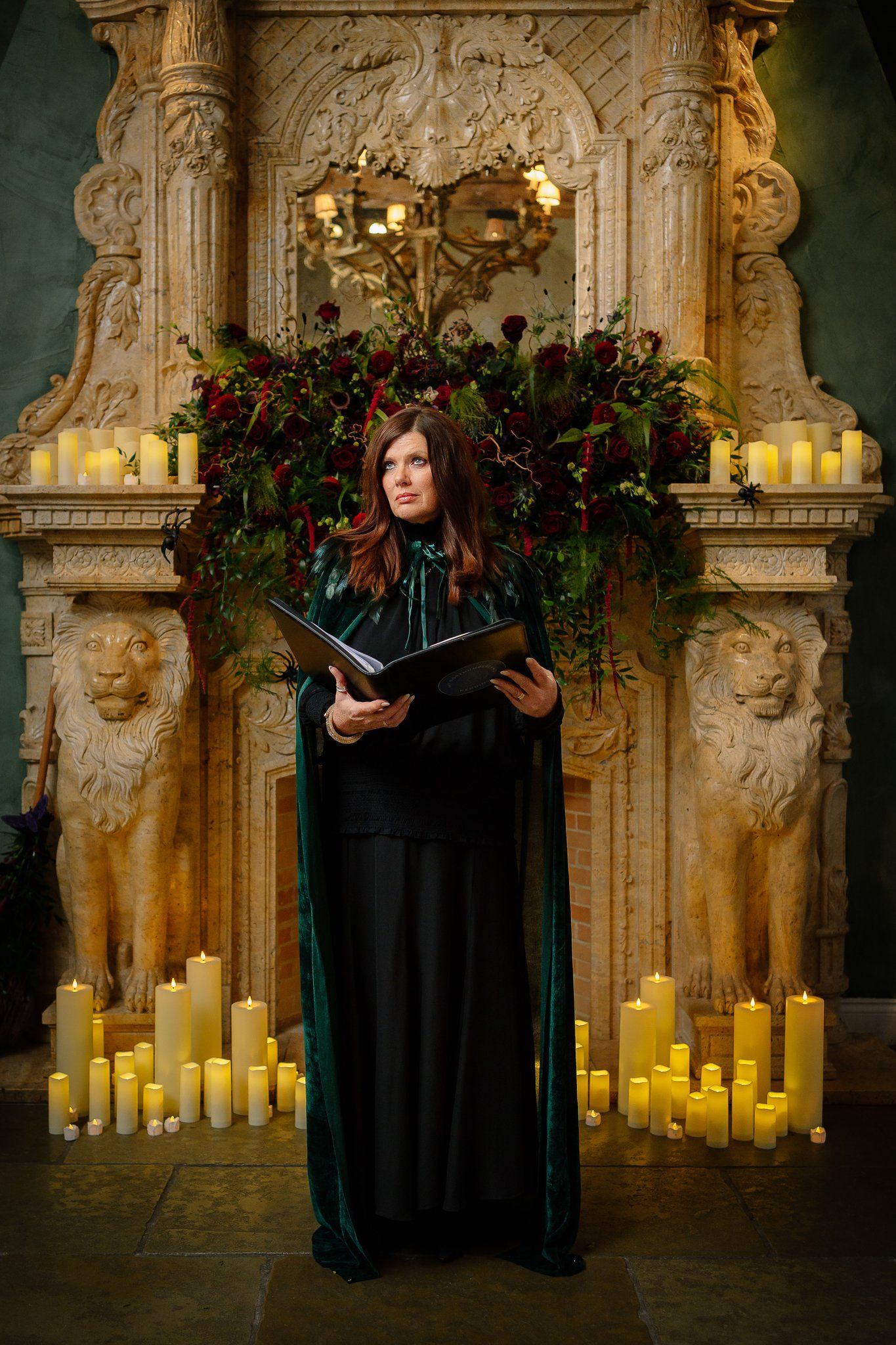 Northumberland Registrar in a green velvet cloak standing before a candlelit fireplace at Le Petit Chateau for a Halloween wedding ceremony