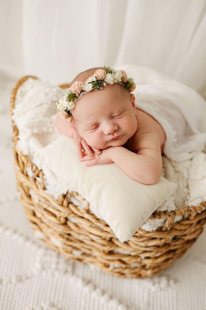 Newborn baby girl with a flower crown resting her head on her hands in a basket, Keli Tetzlaff Photography