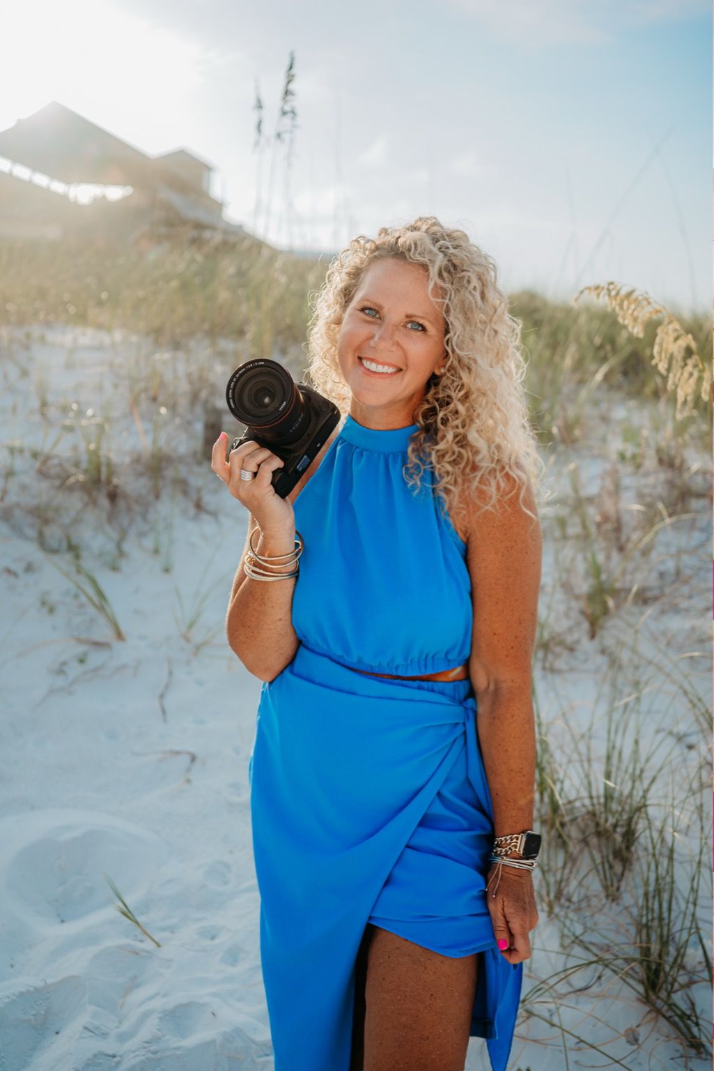 A person in a bright blue dress walks through white sandy dunes with beach grass on a sunny day.