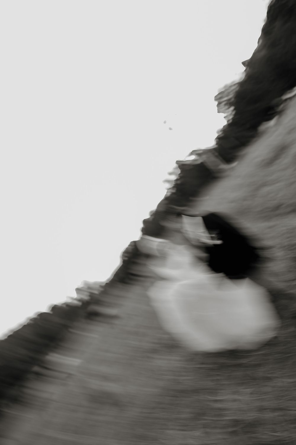 Blurred black and white motion photograph of a figure in white dress on rocky terrain.