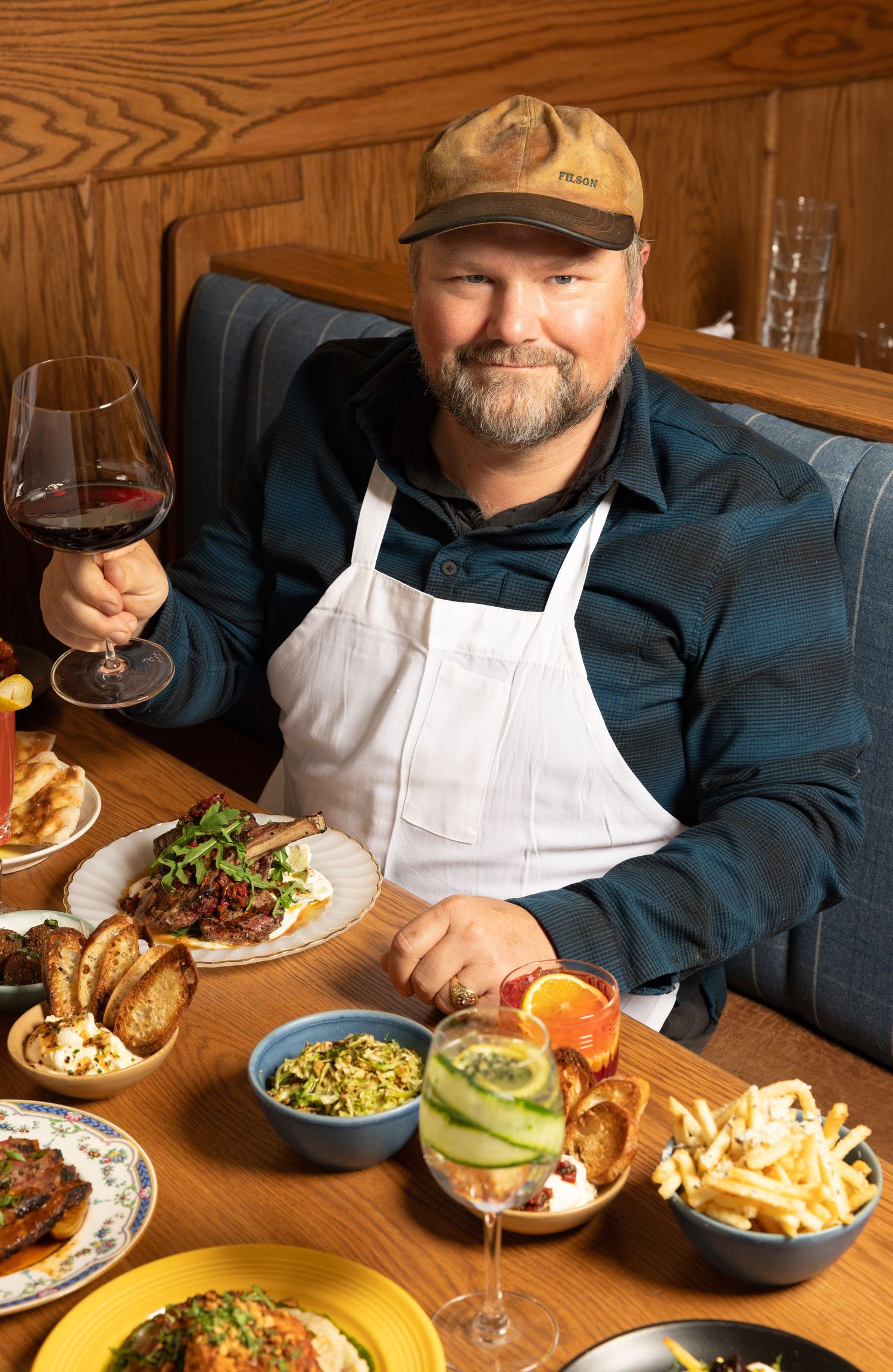 Chef Charlie, Eva's Restaurant pictured seated with a table of food holding a glass of wine.