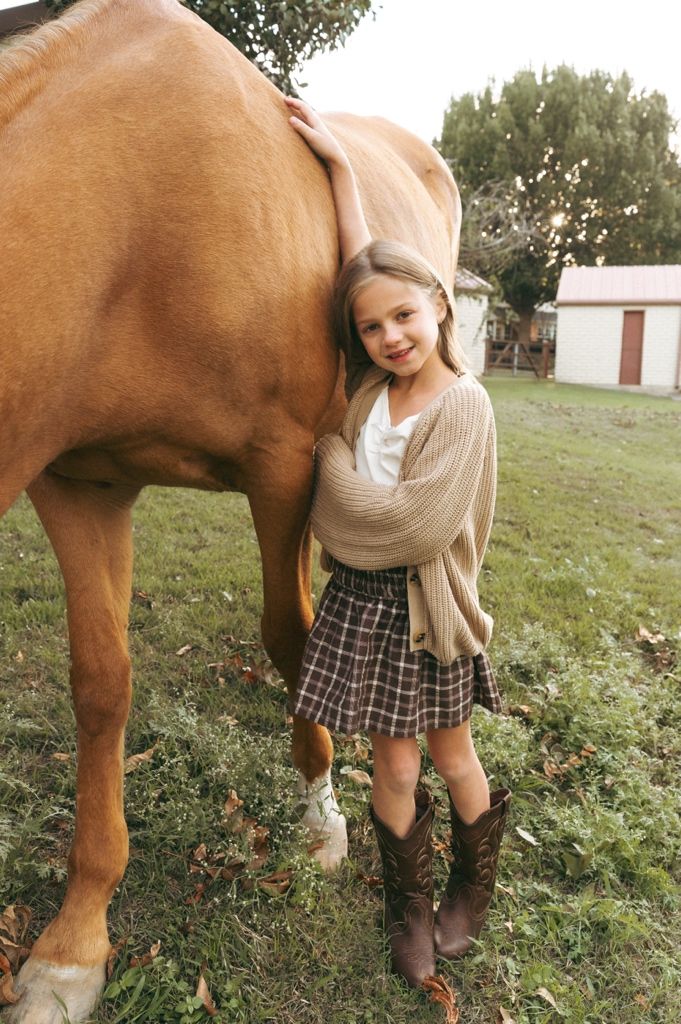 Young girl reaching up to pet a horse during a candid family photography session at Windmill Stables.