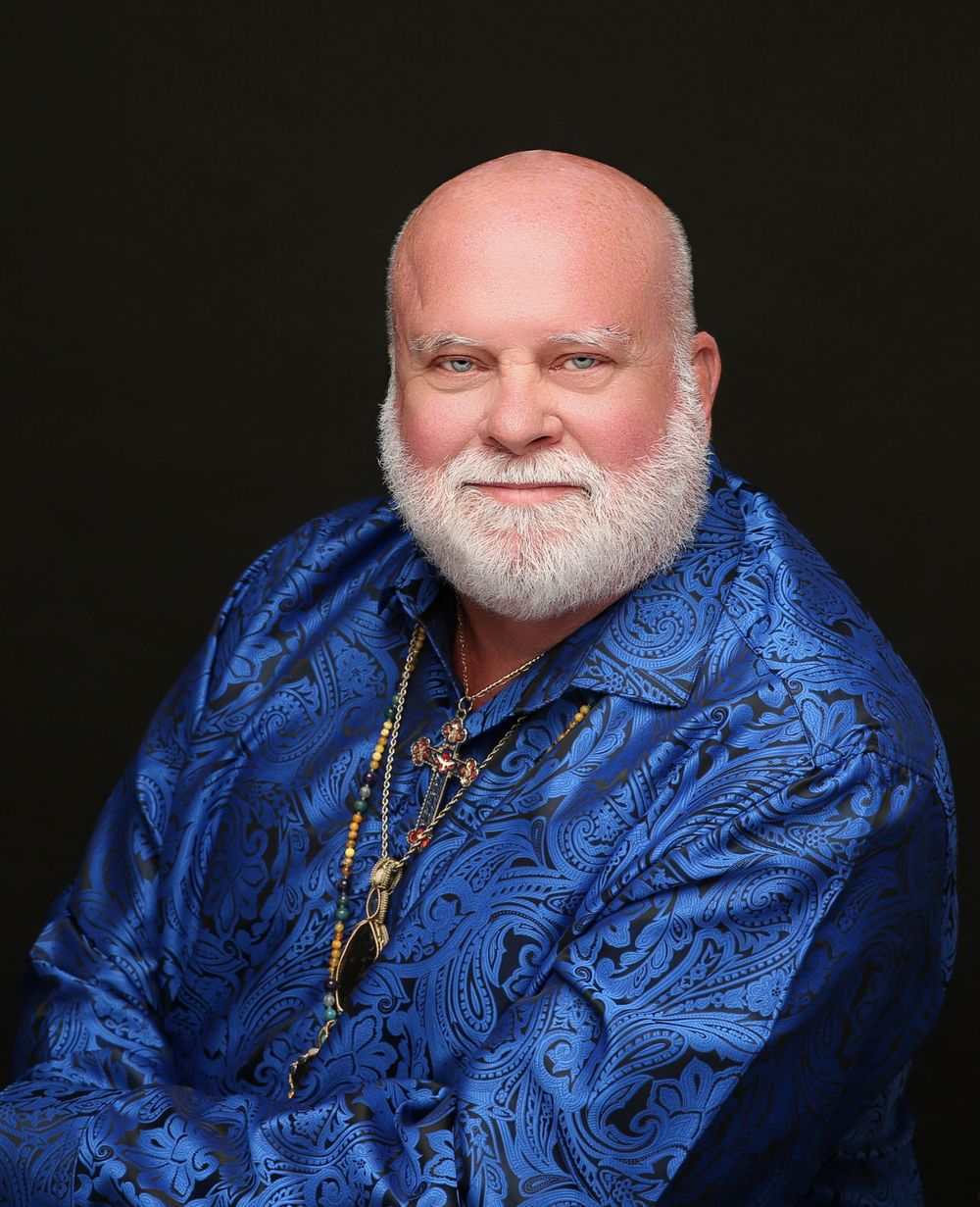Man with a white beard in a royal blue paisley shirt on a black backdrop, creative personal brand headshot