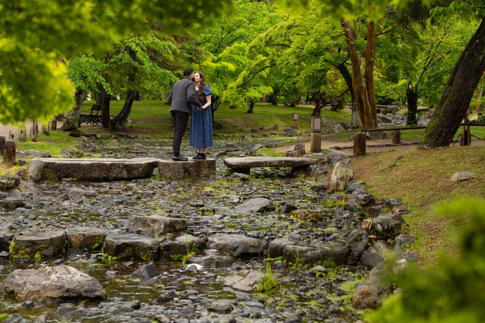 Couple embracing on stepping stones in a lush green Japanese garden with rocky stream bed.